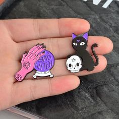 two pins in the palm of someone's hand with a cat and skull on it