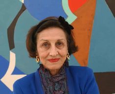 an older woman in front of a colorful wall wearing earrings and a blue blazer