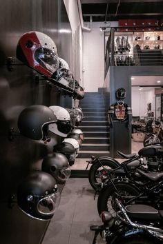 motorcycles and helmets are lined up on the wall in this shop, with stairs leading to the second floor