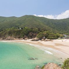 a beach with clear blue water and green hills in the background