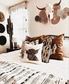 a bed topped with lots of pillows next to a wall mounted cow skull on the wall