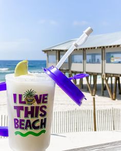 a drink sitting on top of a wooden table next to the ocean with a straw in it