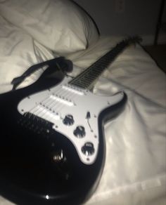 a black and white guitar laying on top of a bed next to a headphone