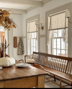 a wooden table sitting in front of two windows next to a bench with plates on it