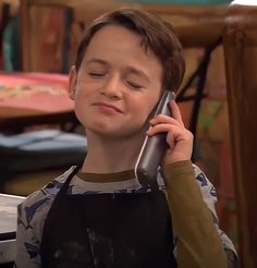 a young boy talking on a cell phone while sitting at a table with his eyes closed