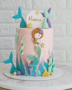 a pink and blue cake with mermaids on it