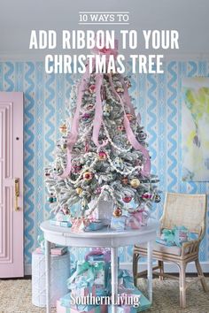 a white christmas tree with pink ribbon and presents under it in front of a blue patterned wall