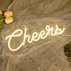 a neon sign that says cheers next to tulips on a sheer fabric background