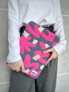 a woman is holding a pink and gray purse with hearts on it, while standing in front of a wall