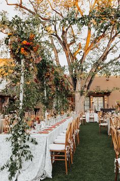 an outdoor dining area with tables and chairs set up for a wedding reception under a tree