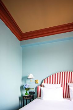 a white bed with red and white striped headboard next to a lamp in a blue room