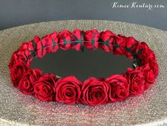 a round mirror with red roses on it sitting on top of a silver tablecloth