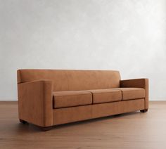 a tan leather couch sitting on top of a hard wood floor next to a white wall