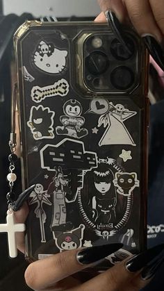 a person holding up a cell phone case with stickers on it and keys in their hands