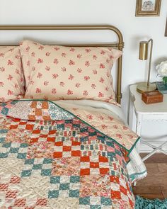 a bed with an orange and blue quilt on it's headboard next to a night stand