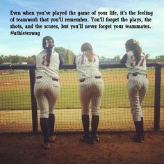 three women in baseball uniforms are standing at the dugout with their backs to the camera