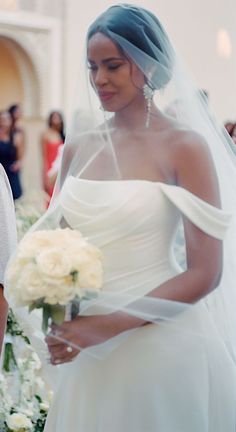 a woman in a white wedding gown and veil walking down the aisle with her bride