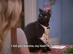 a black cat sitting on top of a table next to a woman in a white shirt