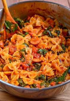 a bowl filled with pasta and spinach on top of a wooden table next to a spoon