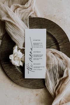 a table setting with an elegant menu card and white flowers on the plate next to it