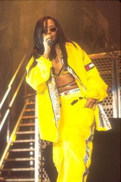 a woman in yellow outfit standing on stage holding a microphone to her ear and singing into a microphone