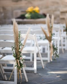 rows of white chairs with flowers and greenery on them