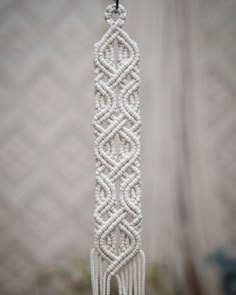 a close up of a white beaded object hanging from a hook on a wall