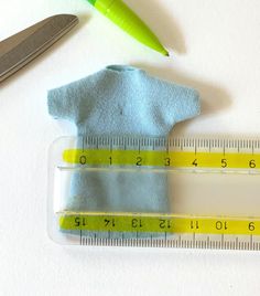 a pair of scissors, measuring tape and blue shirt on a white surface with a green marker