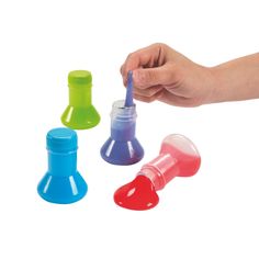 a hand holding a blue toothbrush next to three small plastic bottles with different colors