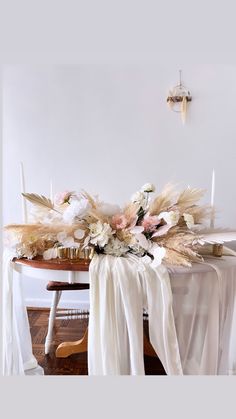 an arrangement of flowers and candles on a dining room table with white draping