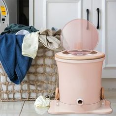 a pink trash can sitting on top of a kitchen floor next to a laundry basket