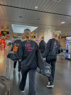 two women in matching sweatshirts pulling luggage through an airport terminal with their back to the camera