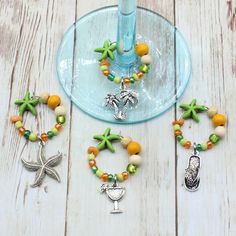 some beads and charms are sitting on a table next to a wine glass with a blue vase in the background