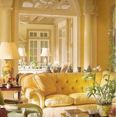 a living room filled with yellow furniture and lots of green plants on top of it