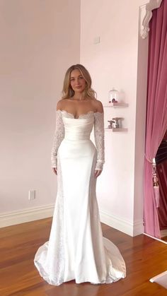 a woman in a white wedding dress standing on a wooden floor next to a pink curtain