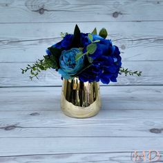 a gold vase filled with blue flowers on top of a wooden table