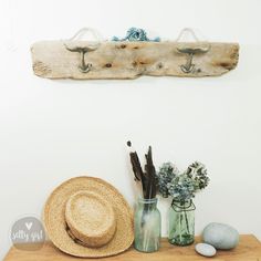 a hat, vase with flowers and other items on a wooden shelf in front of a white wall