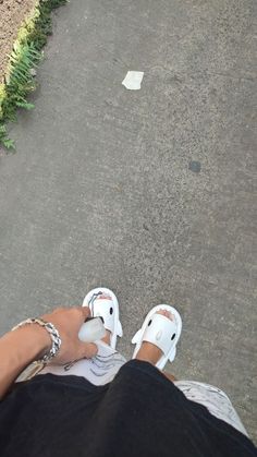 a person sitting on the ground with their feet up and wearing white shoes, holding something in one hand