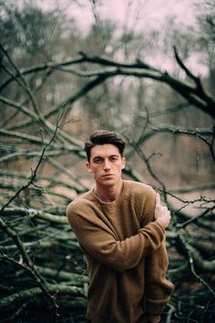 a young man is standing in the woods with his arms crossed and looking at the camera