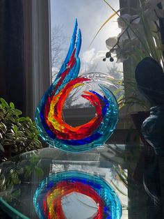 a colorful glass sculpture sitting on top of a table next to a potted plant