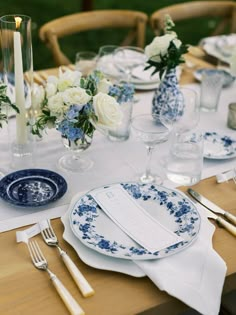 the table is set with blue and white plates, silverware, and flowers in vases