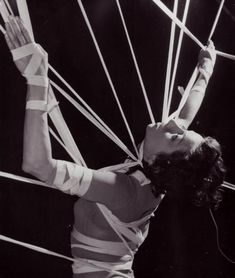 an old photo of a woman holding up some strings in the air with her hands