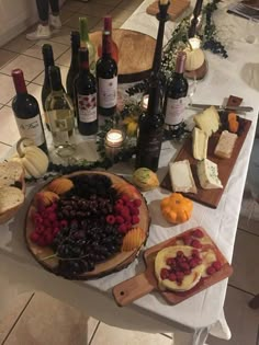 an assortment of cheeses, fruit and wine on a table with bottles of wine