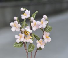 small white flowers with green leaves and a yellow bee on one end, sitting in a glass vase