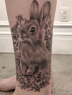 a black and white tattoo of a rabbit on the leg, with flowers around it