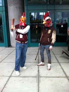 two people dressed as roosters holding baseball bats on the sidewalk in front of a building