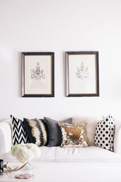 two framed pictures hang on the wall above a white couch with black and gold pillows