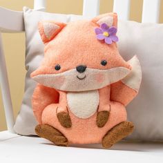 a small stuffed fox sitting on top of a white chair next to a pillow with a purple flower