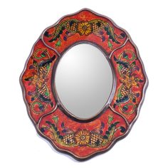 a decorative mirror with an orange and red design on the front, sitting against a white wall