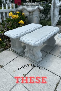 two white benches sitting on top of a cement slab next to yellow flowers and statues